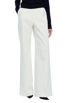A person wearing the Lela Rose Stretch Cotton Molly Pant in white—high-rise, wide-leg pants crafted from stretch cotton—paired with a black long-sleeve top and black shoes, standing against a white background.