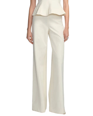 Model in Lela Rose Stretch Cotton Pant, featuring a tailored, high-rise waist in cream, paired with a matching peplum top; photographed from shoulders to feet against a white background.