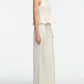 A woman stands in profile against a white background, wearing the Lela Rose Stretch Cotton Halter Top and matching wide-leg pants—a chic off-white cocktail set with tailored fit and flared hem.