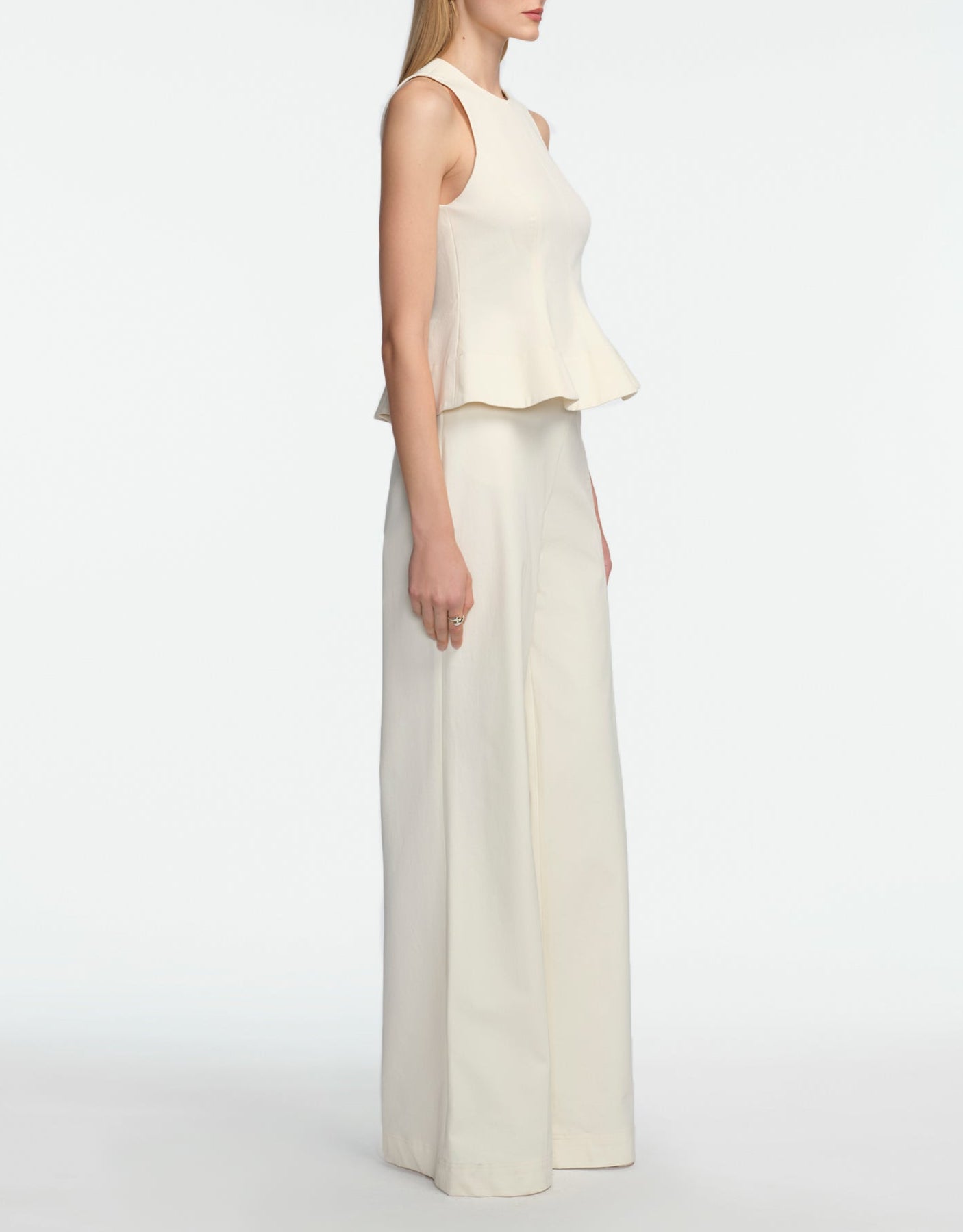 A woman stands in profile against a white background, wearing the Lela Rose Stretch Cotton Halter Top and matching wide-leg pants—a chic off-white cocktail set with tailored fit and flared hem.