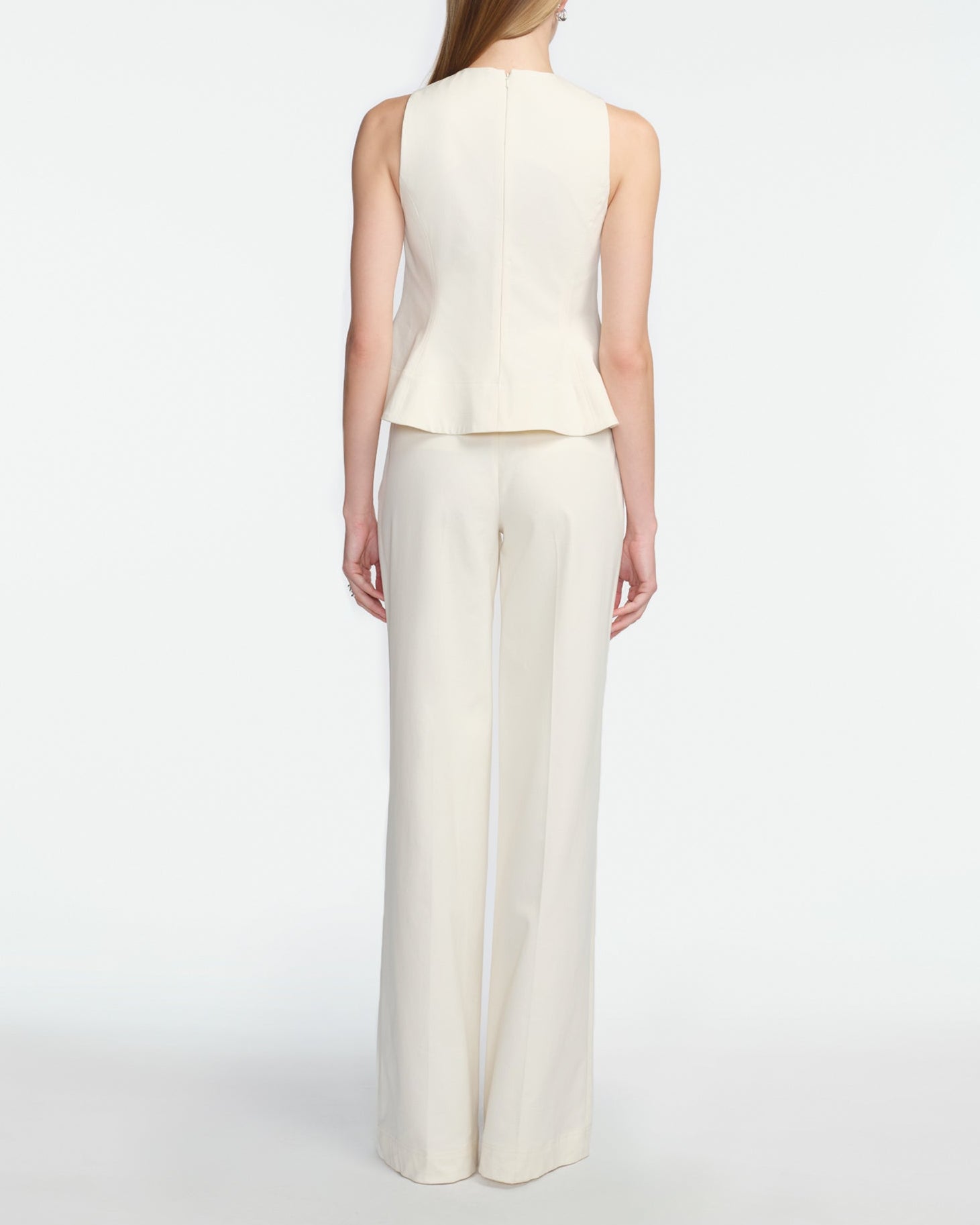 A woman stands facing away in a Lela Rose Stretch Cotton Halter Top, off-white with tailored fit and flared hem, paired with matching wide-leg trousers against a plain white background.