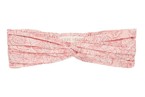 The Julie Headband by Louise Misha is a light pink cotton batiste turban with a delicate floral pattern and stylish front twist, shown laid flat on a white background.
