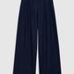 The Lou Trouser by Anine Bing features wide-leg, dark blue cotton denim with a high-rise trouser fit and pleated detailing, shown laid flat on a light gray background—reflecting Anine Bing’s signature style.
