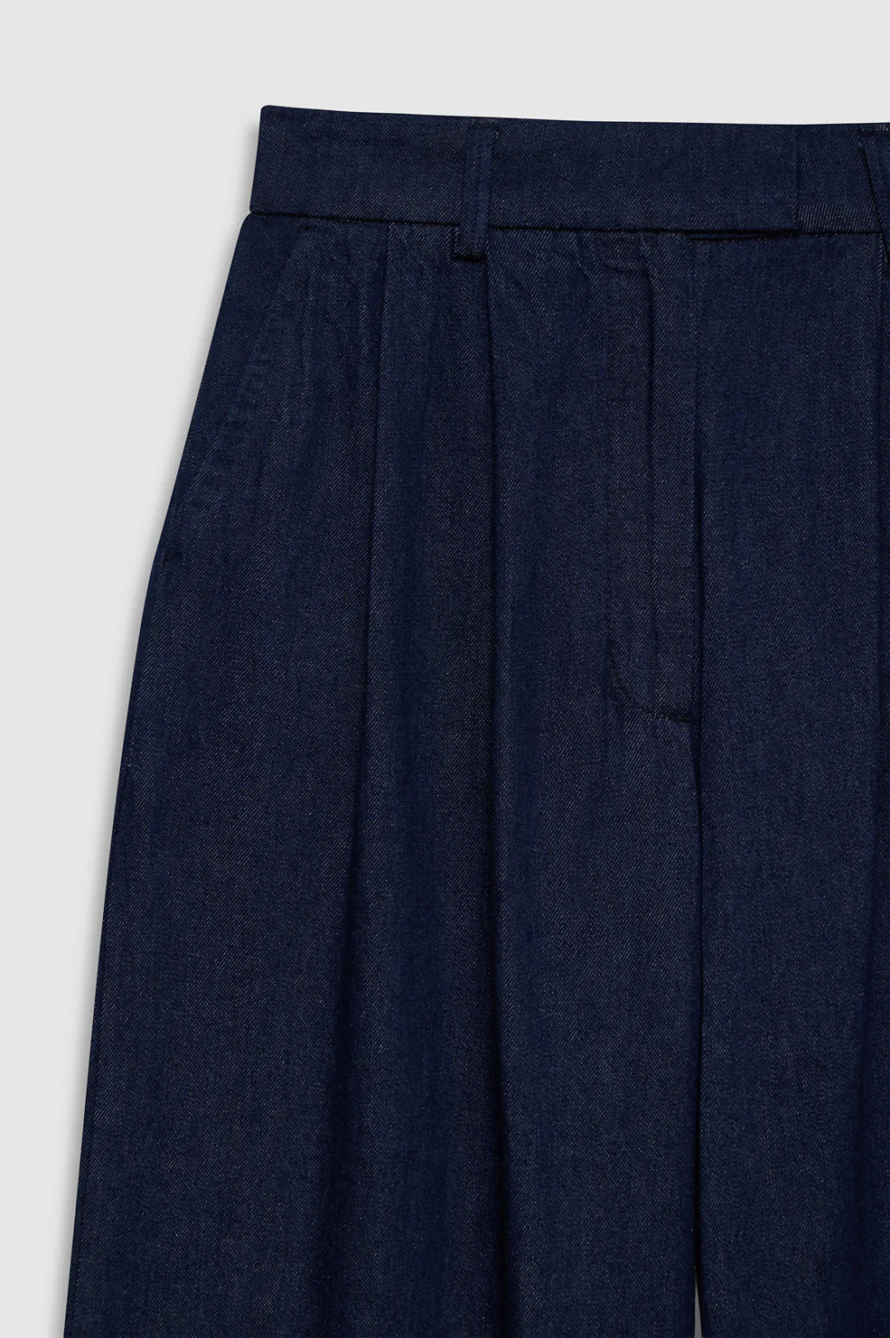 Close-up of the Lou Trouser by Anine Bing in dark blue cotton denim, showcasing a high-rise waistband with belt loops, pleated front detail, and side pockets, photographed against a plain light background.
