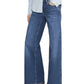 Person wearing a light blue button-up shirt, Frame Low Rise Le Slim Palazzo women's jeans, and brown heeled shoes, standing against a white background.