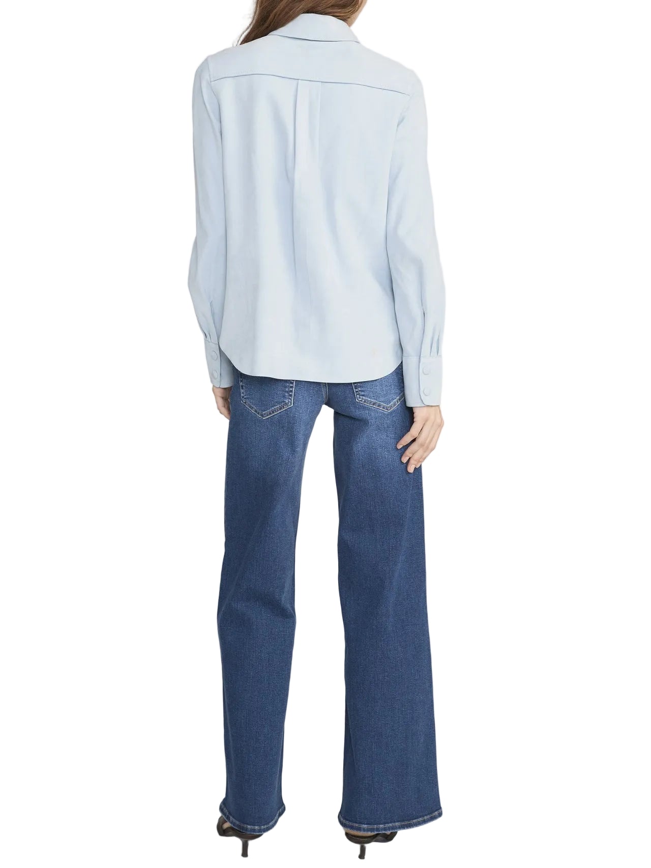 A person stands with their back to the camera, wearing a light blue long-sleeve shirt, blue Low Rise Le Slim Palazzo jeans by Frame, and black shoes.