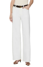 Person wearing Frame’s Le Slim Palazzo high-waisted white wide-leg pants, a black belt, strappy brown sandals, and a sleeveless top, with one hand in the pocket.