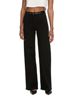 A person wears Frame’s Le Slim Palazzo high-rise, wide-leg black jeans with a black belt, white crop top, and black pointed shoes, standing against a plain background.