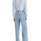 A person stands facing away in a light blue button-up shirt, Frame’s Le Slim Palazzo high rise light blue jeans crafted from sustainable cotton, and beige pointed shoes against a plain background.