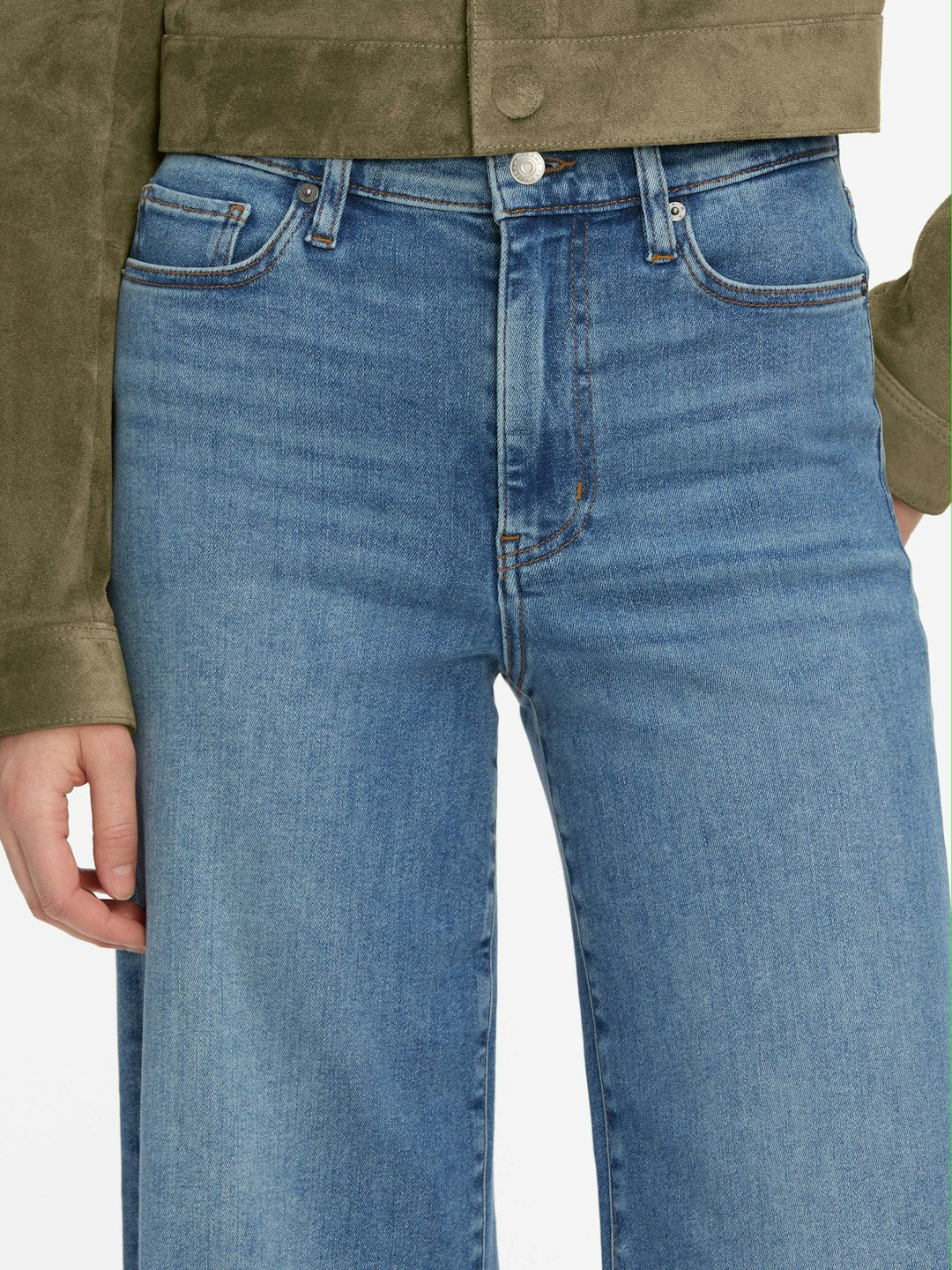 Model wearing Frame's Le Slim Palazzo high-rise blue jeans, featuring a subtle palazzo silhouette, paired with a green suede jacket; shown from mid-torso to upper thighs with one hand at their side.