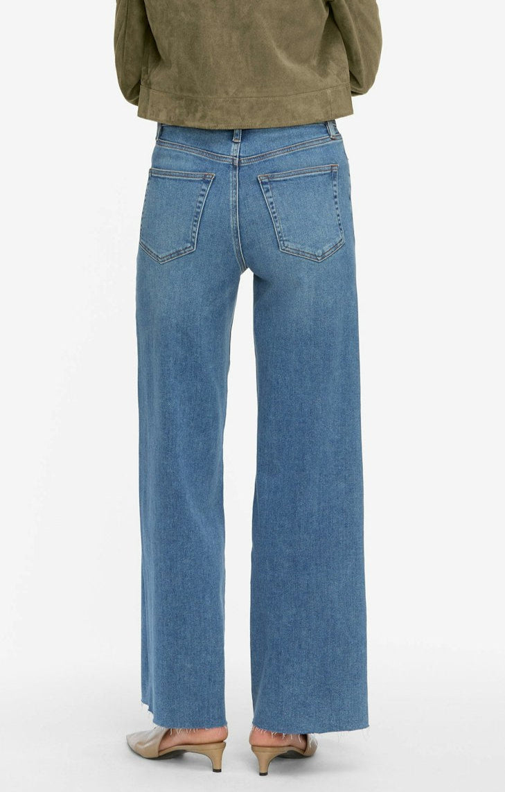 A person shown from the back, standing on a white background, wears Frame's Le Slim Palazzo high-rise, wide-leg flare blue jeans with raw hems and an olive-green jacket.