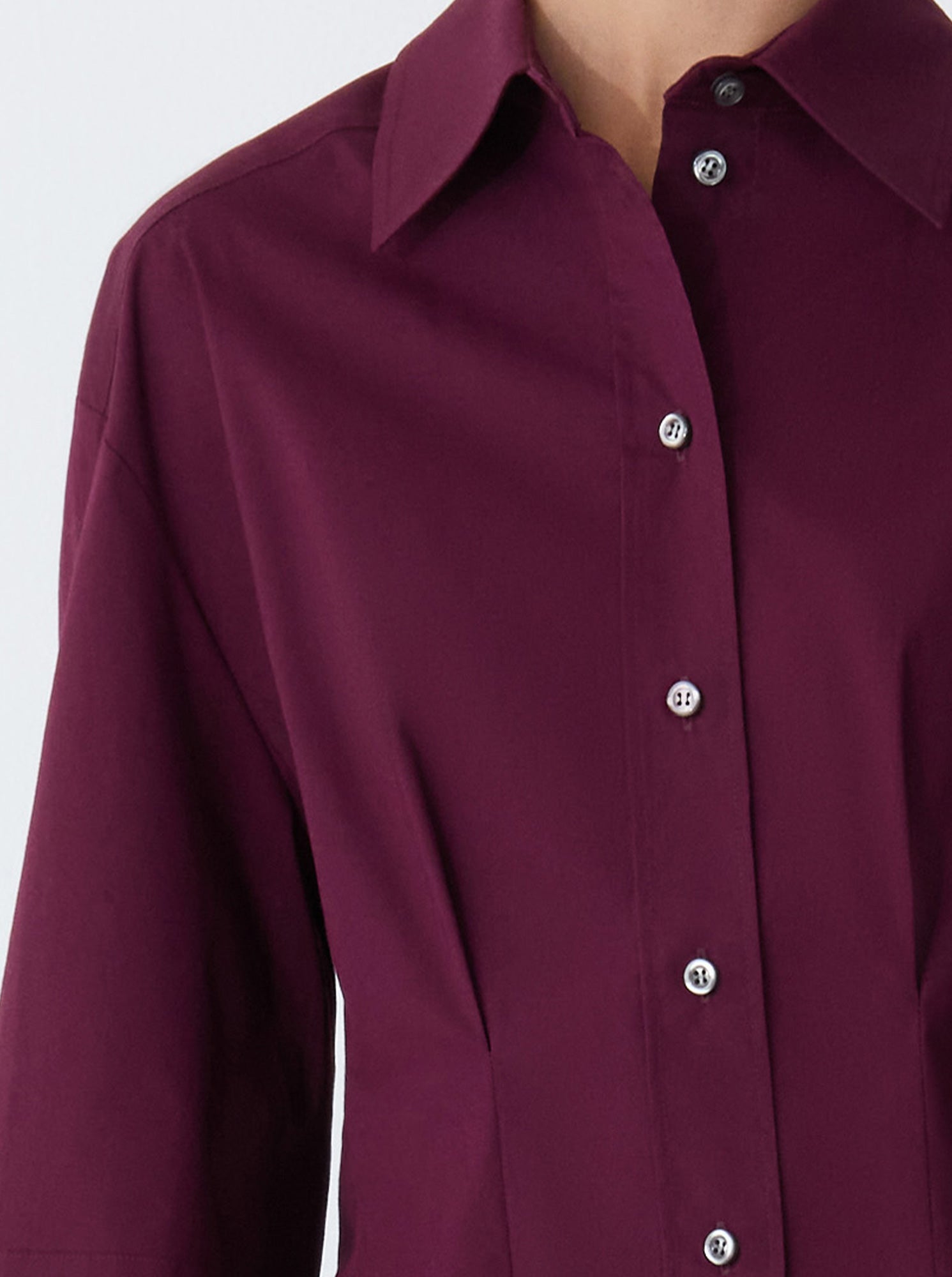 A person wearing the Callas Milano Lucia Top, a maroon cotton poplin button-up shirt with a collar, shown from shoulders to waist.