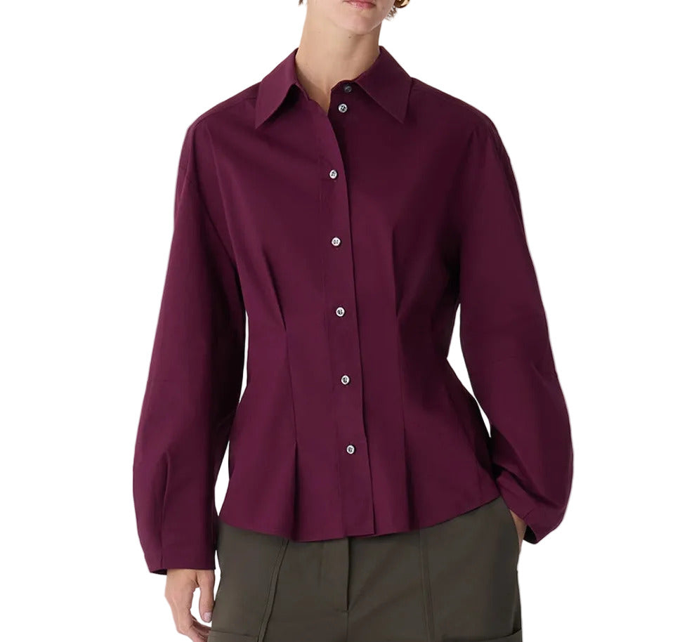 A person wearing the Lucia Top by Callas Milano—a dark purple, long-sleeve, button-front cotton poplin blouse with a collar—paired with olive green pants.