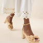 A person wears the Loeffler Randall Lucia Platform sandals, which feature a tan block heel and knotted bows, paired with a white dress that has decorative cutouts at the hem.