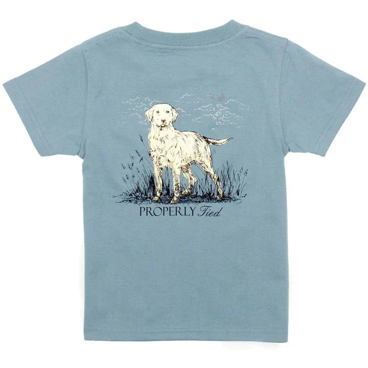 Properly Tied Boys Labrador SS Tee showcases a delightful illustration of a white dog standing in grass, with "PROPERLY Tied" written beneath it. This classic design seamlessly blends style and comfort, making it a must-have addition to any wardrobe.