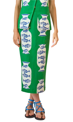 A person models the Hunter Bell NYC Isla Skirt in Herring Green with blue and white fish vase motifs, styled with blue rope sandals. The linen-blend skirt is shown in a photo cropped from the shoulders down.