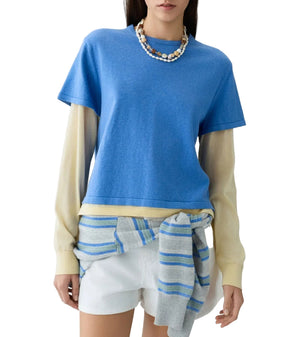 A woman styles the Guest in Residence Layer Tee over beige undersleeves, with white shorts, a striped sweater tied at her waist, and a beaded necklace for an effortlessly layered look.