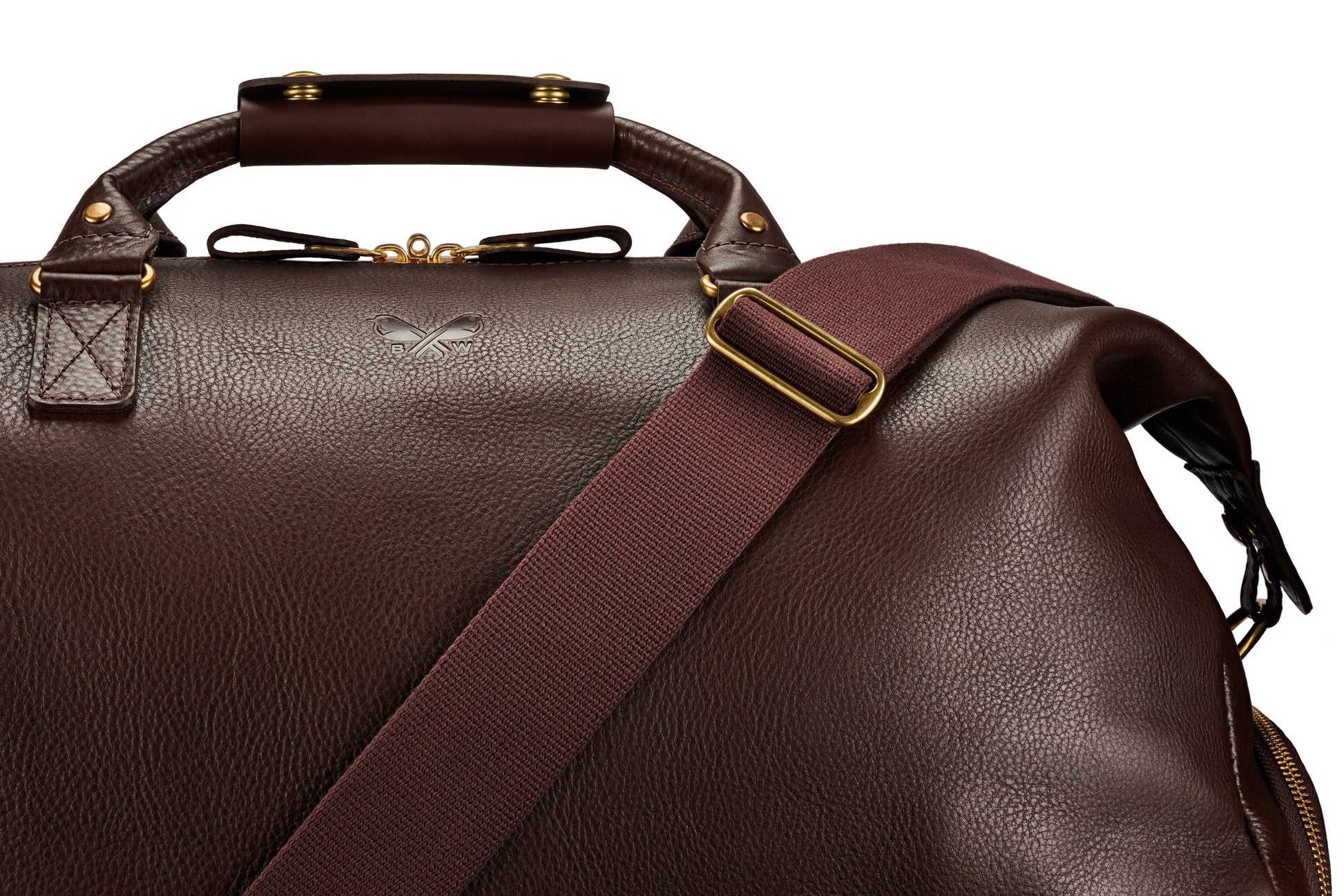 Close-up of the Bennett Winch Leather Weekender, crafted from full-grain leather. The bag showcases a dark brown handle and adjustable strap. Its gold hardware and subtly embossed logo enhance the textured surface, making it an ideal luxury travel accessory.