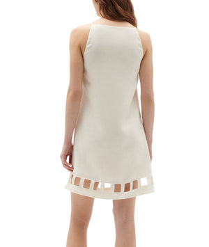 A woman is seen from the back wearing the Figue Leonie Dress, a sleeveless, cream-colored dress with a squared neckline and square cut-out details near the hem. The shift style silhouette of the linen fabric adds an effortless elegance to her look.