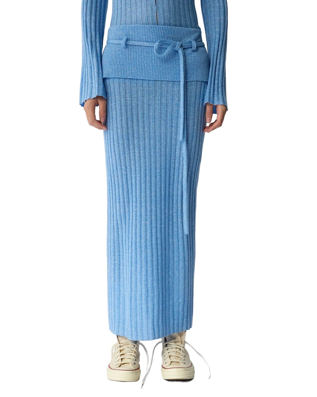 Someone wearing the Guest in Residence Lia Skirt—a blue ribbed knit design with a fold-over waist and matching tie belt—paired with cream lace-up sneakers.