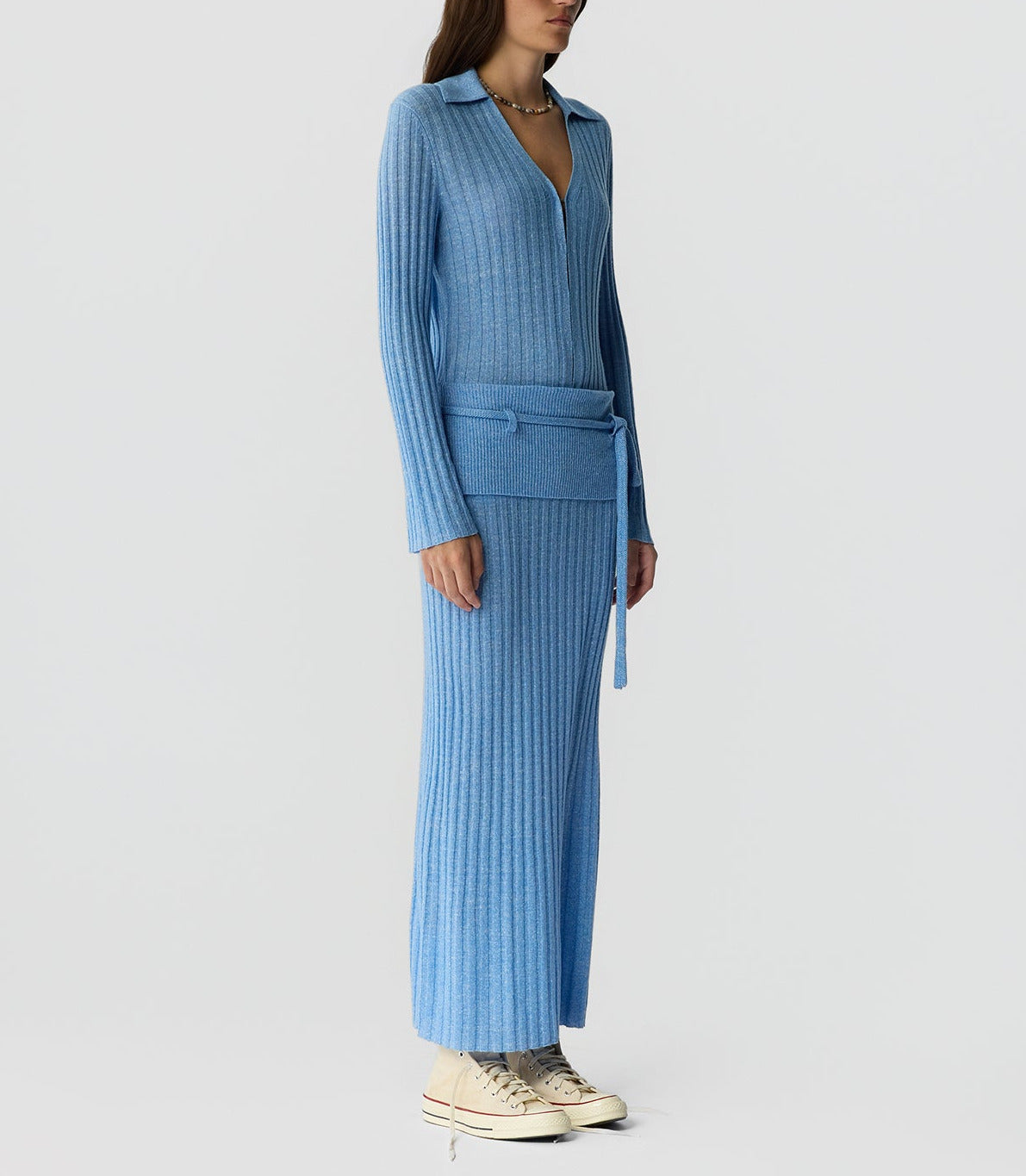 A person models the Lia Skirt by Guest in Residence—featuring an elegant ribbed texture—in light blue, styled with a collar top and beige sneakers against a plain background.