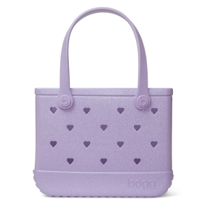 The Bitty Bogg Bag - Shimmer, from Bogg Bags, is a charming purple tote bag featuring heart-shaped cutouts and two sturdy handles. It's perfect for Mommy and Me outings or as a cute alternative for Bogg lovers.