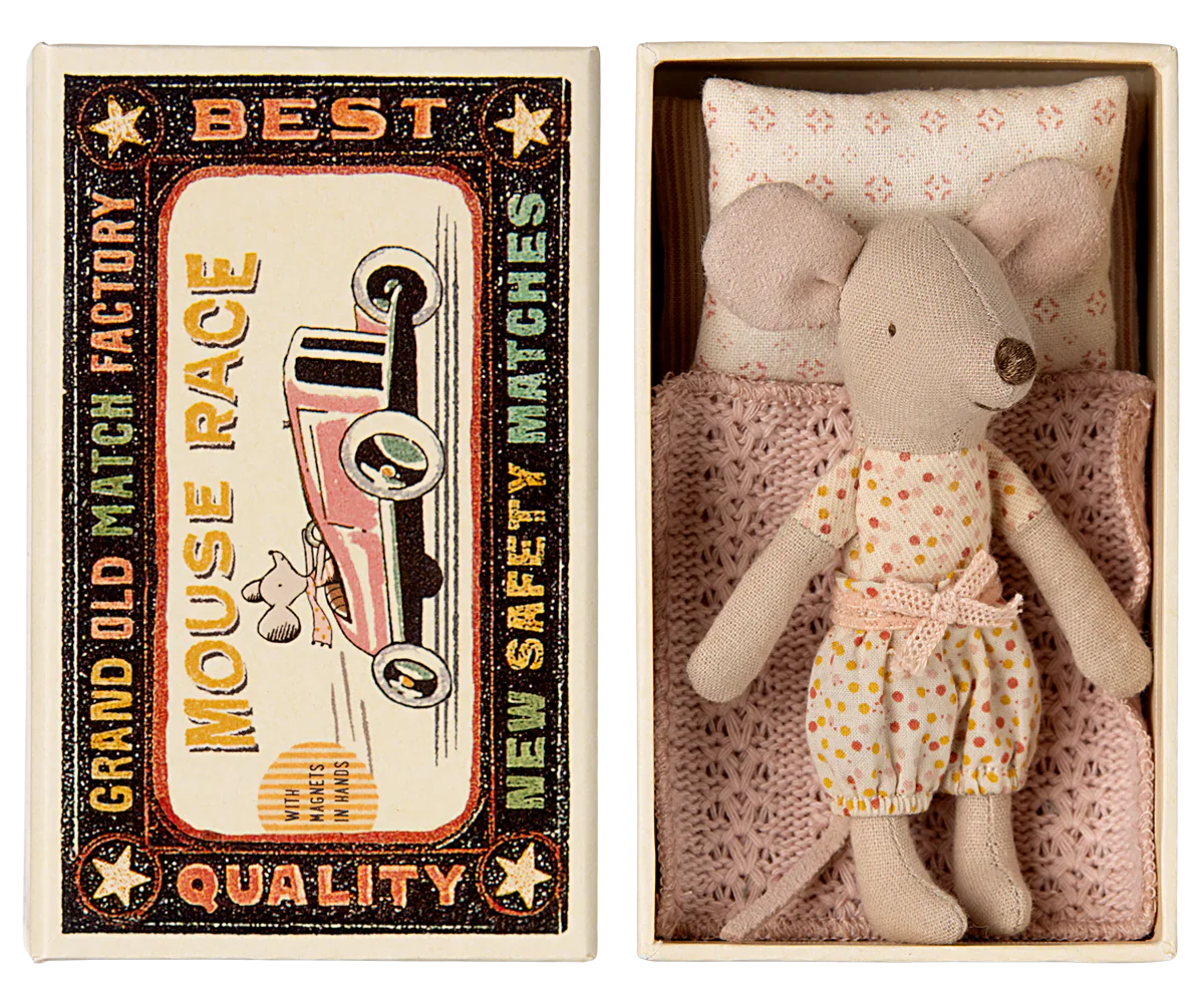 A Maileg Little Sister mouse, dressed in a charming polka-dot outfit, rests comfortably in a matchbox bed crafted from soft fabrics, nestled inside a cardboard box. The box is labeled "Maileg Little Sister, Mouse in Matchbox" and features delightful vintage matchbox-style graphics on the lid.