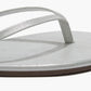 Close-up of the Tkees Lily Glitters Sandals—a silver metallic flip-flop featuring a thin strap, cushioned insole, and flat sole—shown on a white background.