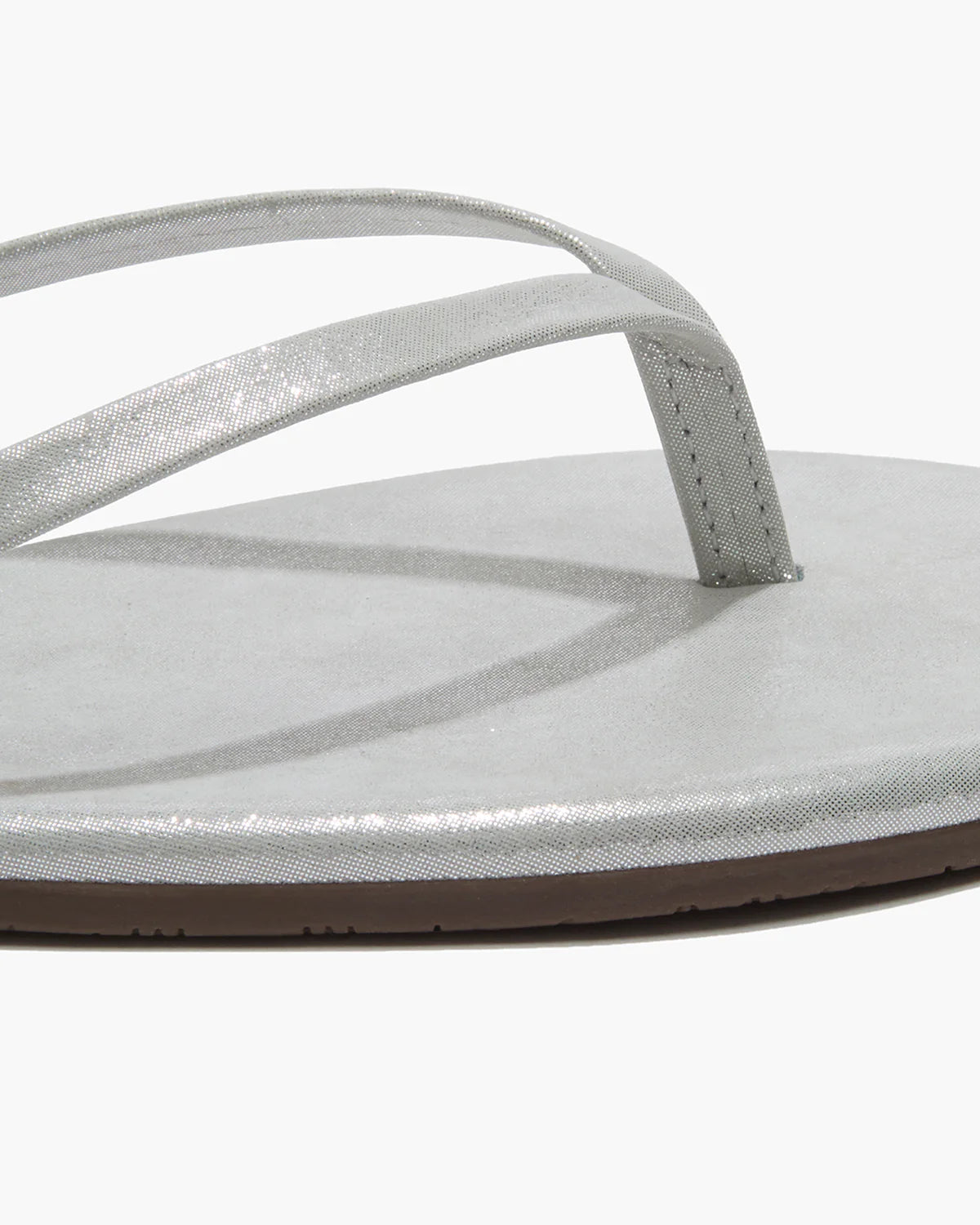 Close-up of the Tkees Lily Glitters Sandals—a silver metallic flip-flop featuring a thin strap, cushioned insole, and flat sole—shown on a white background.