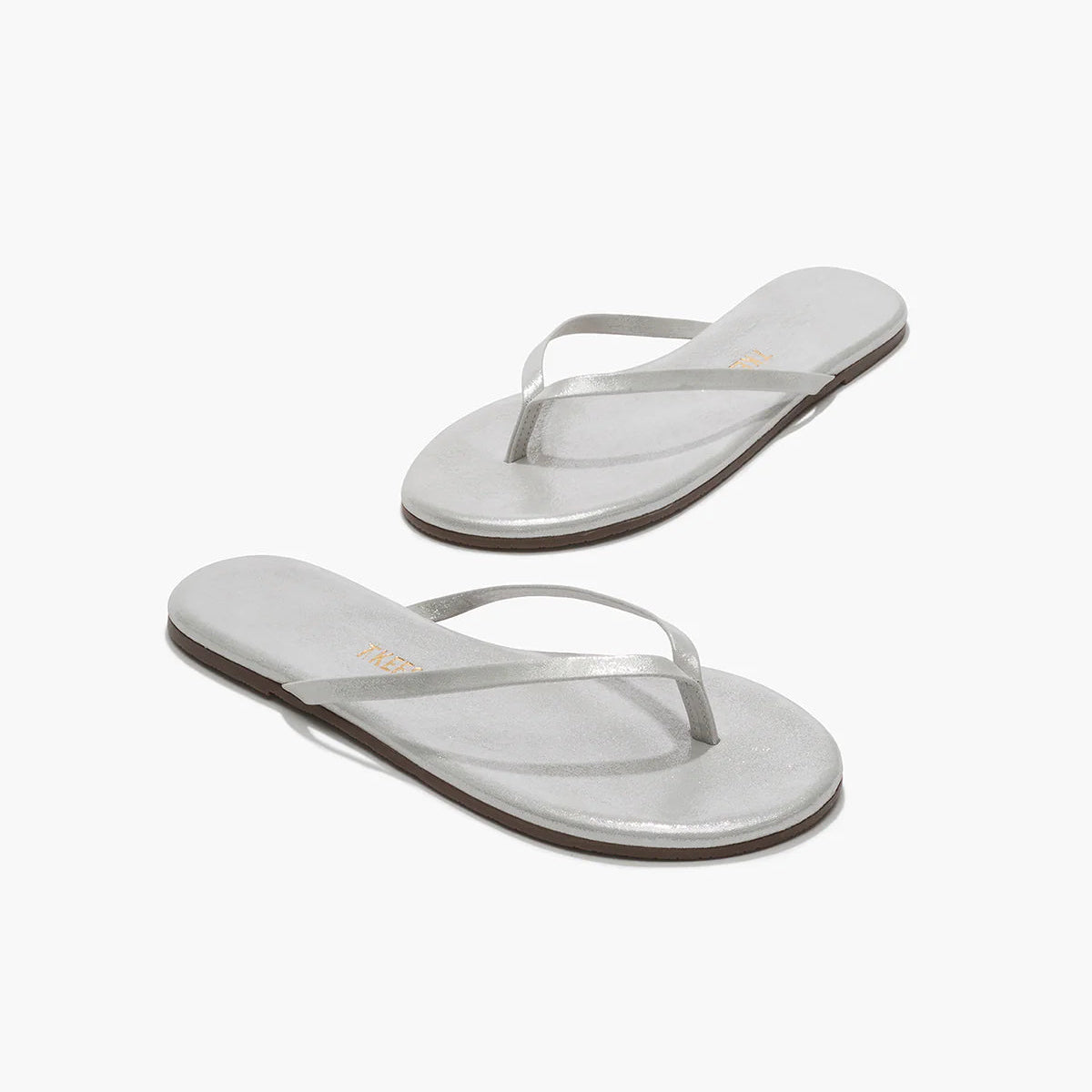 The Tkees Lily Glitters Sandals feature silver glittery thin straps, flat soles, and a cushioned insole for extra comfort, showcased on a white background.