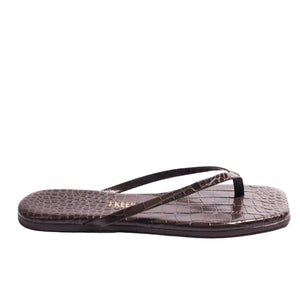 The Tkees Lily Square Toe Croc Sandal is shown in side profile, featuring brown crocodile-embossed leather with thin straps and a square toe.