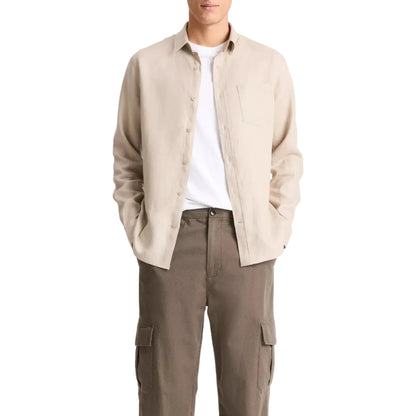 A person wears the vince Linen Longsleeve Shirt in beige over a white tee with brown cargo pants, hands in pockets against a white background—a breathable comfort wardrobe staple.