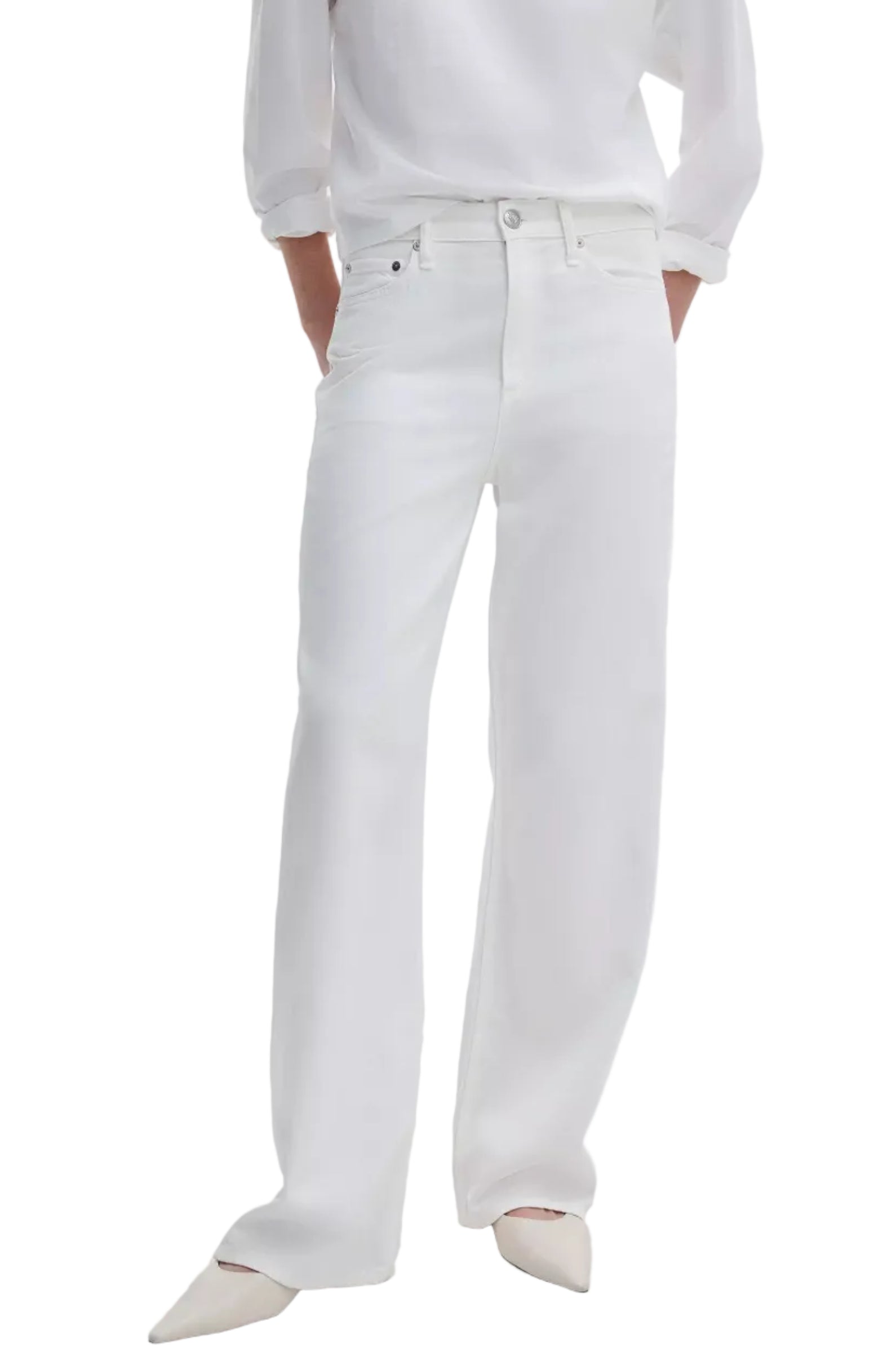 Person wears Rag & Bone Featherweight Logan Wide jeans in white, paired with a white long-sleeve shirt and white pointed-toe shoes, standing with hands in pockets.
