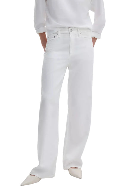 Person wears Rag & Bone Featherweight Logan Wide jeans in white, paired with a white long-sleeve shirt and white pointed-toe shoes, standing with hands in pockets.