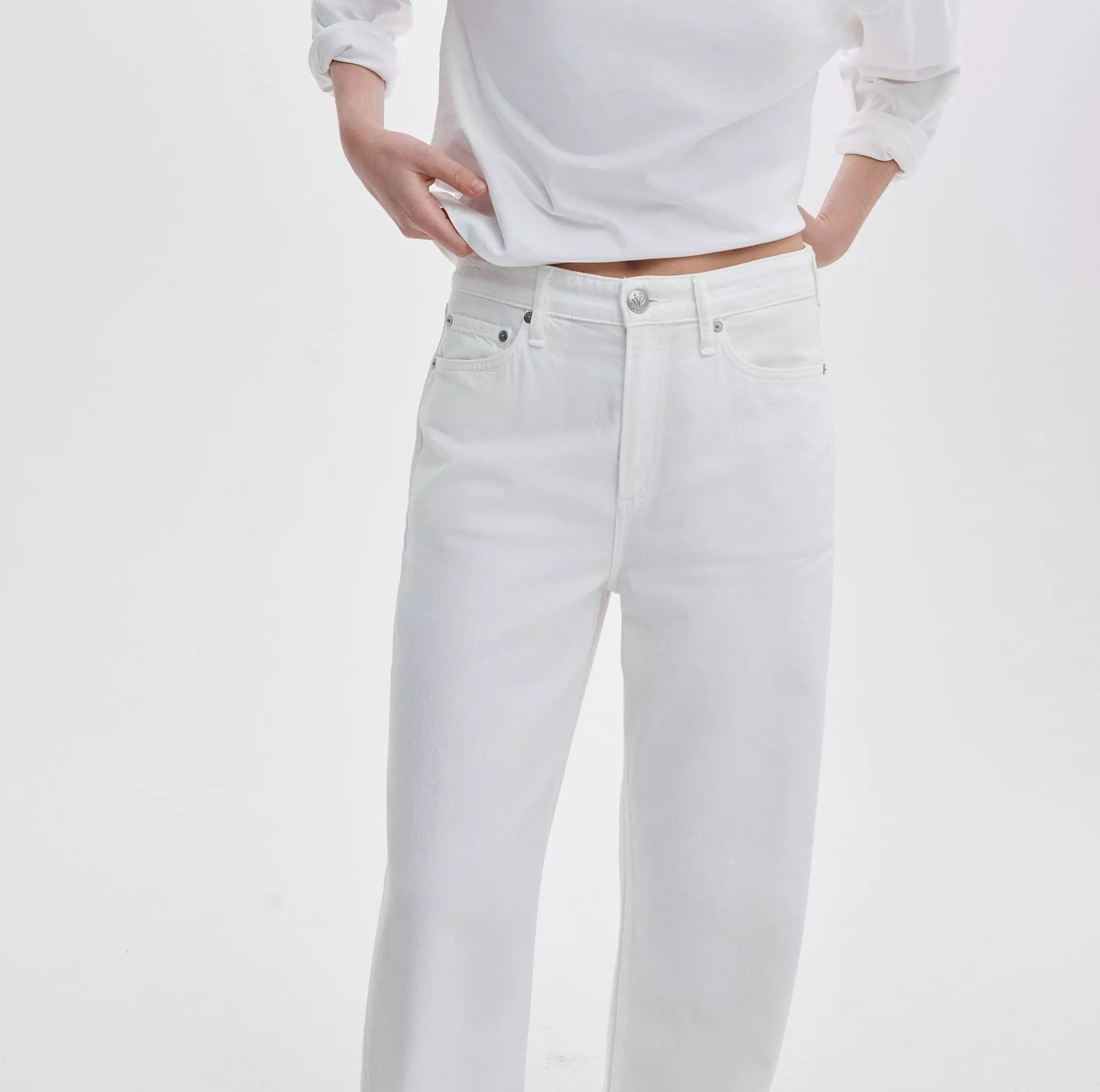 Wearing the Rag & Bone Featherweight Logan Wide jeans, a person poses with one hand on their hip, dressed in a white long-sleeve shirt against a plain white background.