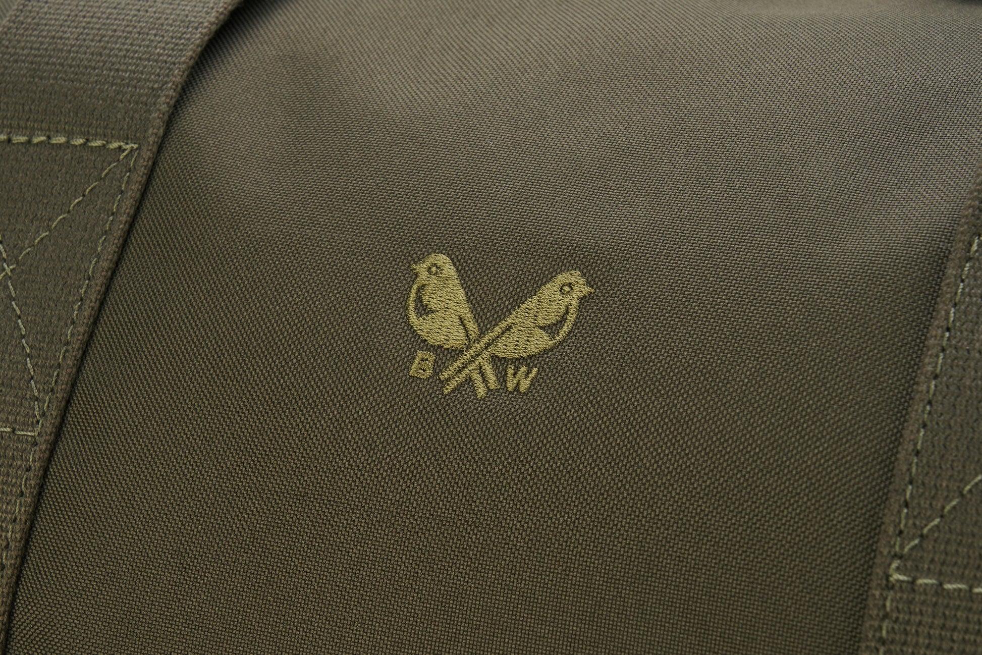 Close-up of a fabric from the Bennett Winch Medium Cargo, featuring two birds perched on branches with the letters "B" and "W" beneath, crafted from waterproof nylon for durability.