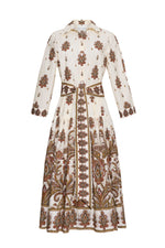 The Lolita Dress by Cara Cara is a long-sleeve, collared shirtdress in white, adorned with brown, rust, and olive paisley border print and floral patterns. It features a button-front closure, fitted waist, and a mid-length skirt.