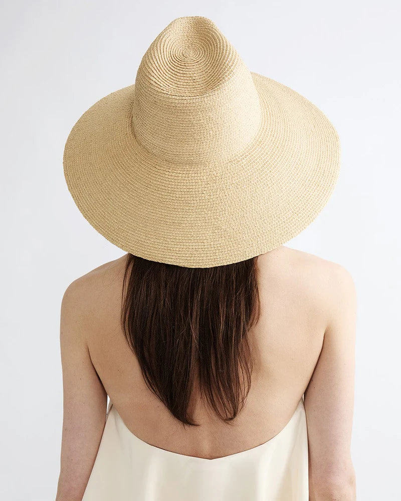 A person with long brown hair, wearing a light strapless top and the Janessa Leone Colette Hat, is seen from behind against a plain background.