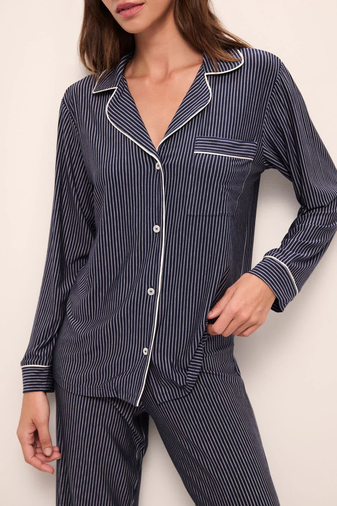 An individual is seen in the Eberjey Tencel Modal Long PJ Set by Eberjey, a dark blue pinstriped pajama set with white piping detail. Featuring a button-up top and matching bottoms made from luxurious knit fabric, this sleepwear offers unparalleled comfort.