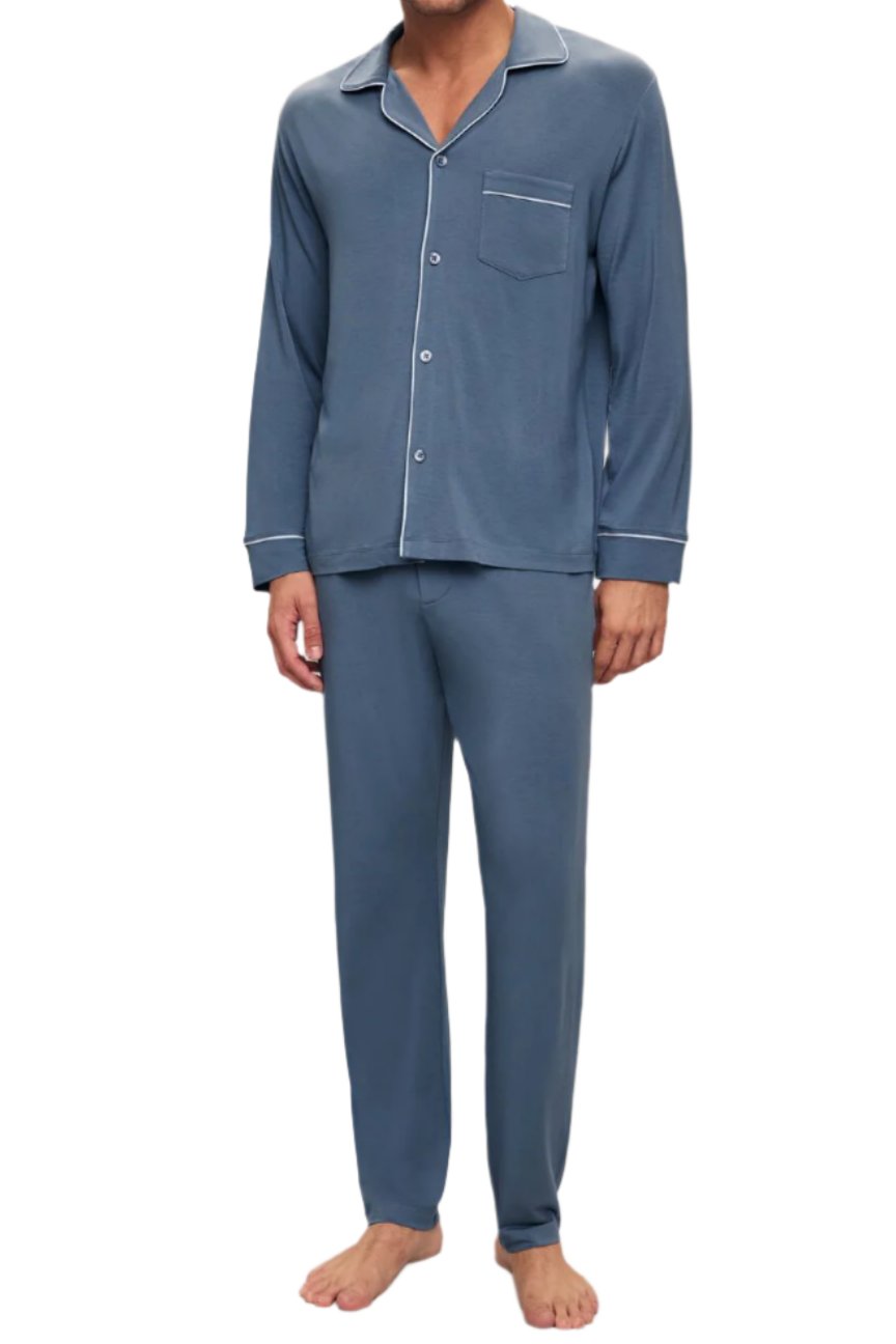 A person in Eberjey's Willam Long PJ Set stands barefoot, donning men's sustainable TENCEL™ Modal blue pajamas with white piping and buttons. The stylish set includes a long-sleeve shirt with a pocket and matching pants, ensuring temperature-regulating comfort.