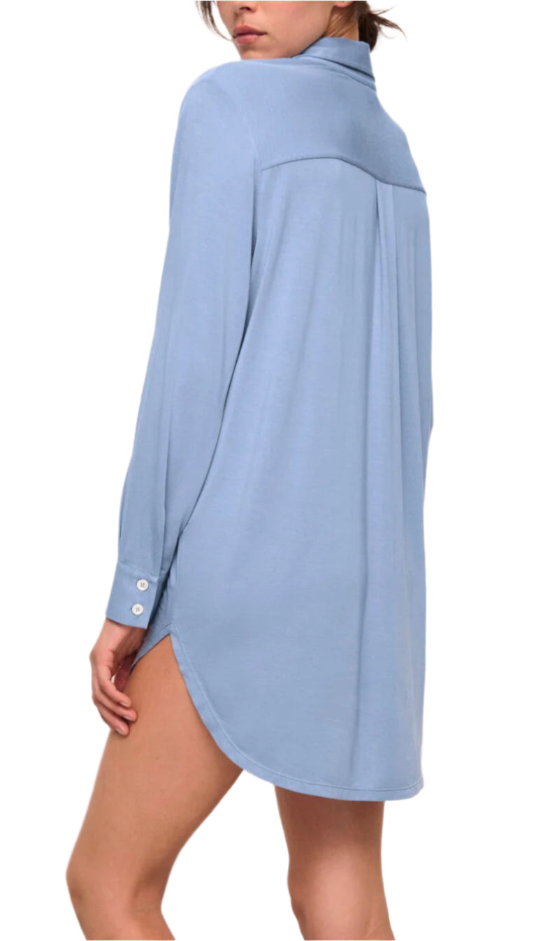 A person wears the Eberjey Gisele Boyfriend Sleepshirt, a light blue, long-sleeve, loose-fit shirt made from sustainable TENCEL™ Modal, with a curved hem and button front that extends to the upper thighs for comfort.