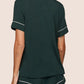 A person faces away, wearing the Eberjey Gisele Relaxed Short PJ Set—a dark green, short-sleeve pajama top and matching shorts with white trim—against a plain light background.