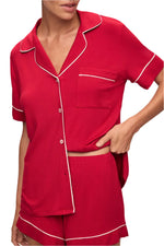 The individual is dressed in the Eberjey Gisele Relaxed Short PJ Set, a luxurious knit fabric set in red with white trim. It includes a short-sleeve button-up top and shorts, crafted from TENCEL™ Modal for exceptional softness and easy maintenance as it is machine washable.