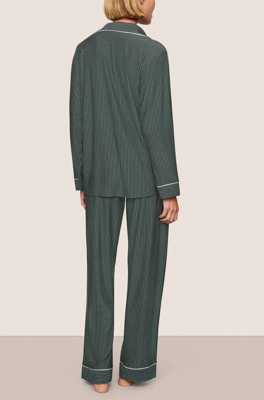 A person stands barefoot facing away against a plain light background, wearing the Eberjey Gisele Printed Stripe Long PJ Set in dark green pinstripes.