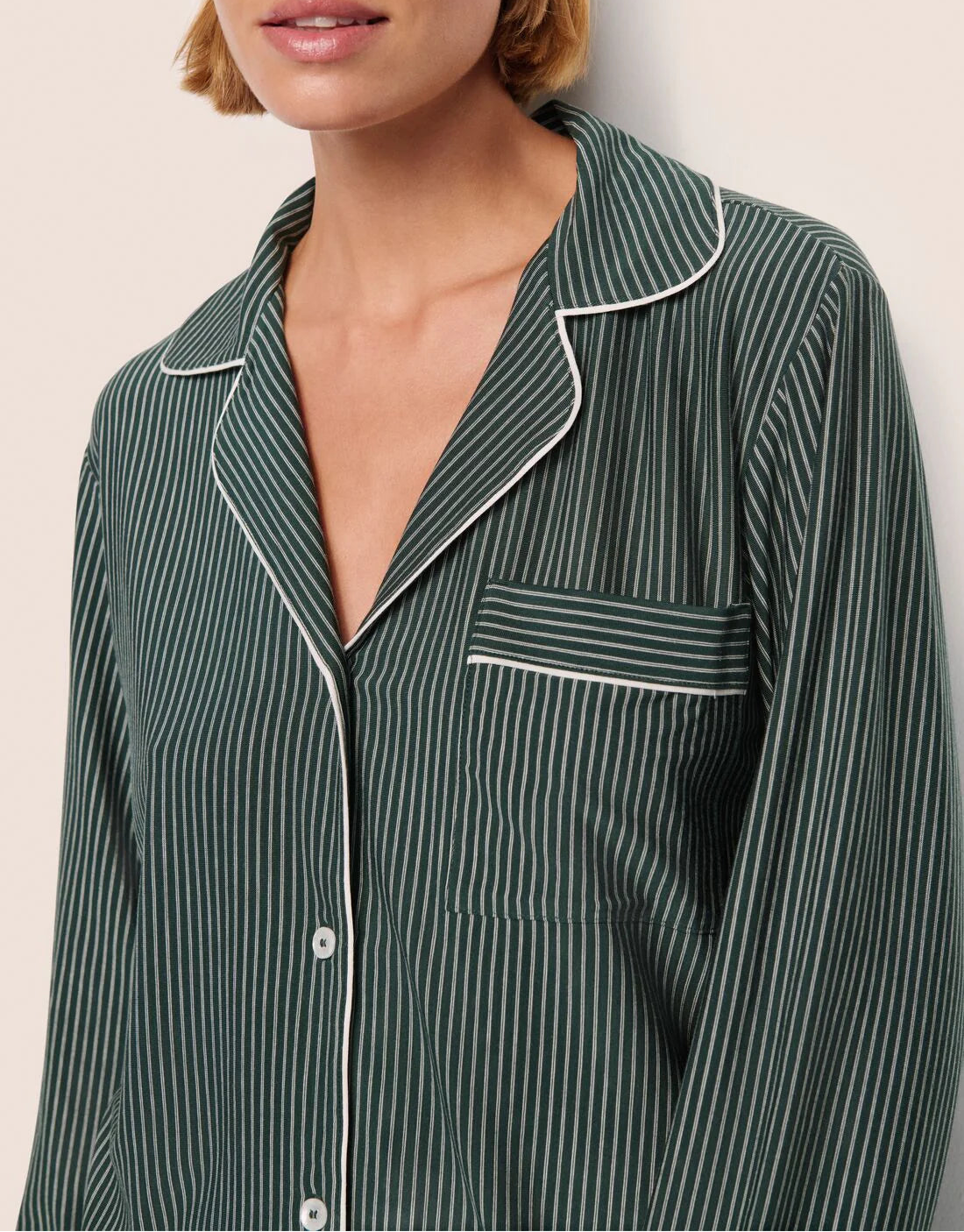 A person wearing the Eberjey Gisele Printed Stripe Long PJ Set in dark green with pinstripes, featuring white piping and a breast pocket, shown from shoulders to mid-chest.