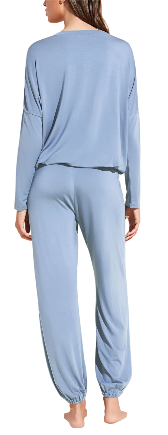 A person wearing the Eberjey EBJ Gisele Slouchy Set—soft, sustainable TENCEL™ Modal pajamas in loose-fitting, light blue long-sleeve top and matching pants—stands barefoot against a white background, shown from the back.