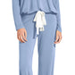 A woman stands barefoot wearing the Eberjey EBJ Gisele Slouchy Set—a loose-fitting, long-sleeve light blue pajama set with cuffed ankles and a white waist tie, made from sustainable TENCEL™ Modal.