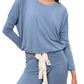 A woman wears the Eberjey EBJ Gisele Slouchy Set, a light blue, long-sleeve lounge set with wide sleeves, a white tie belt at the waist, and temperature-regulating knit fabric, standing with one hand on her hip.