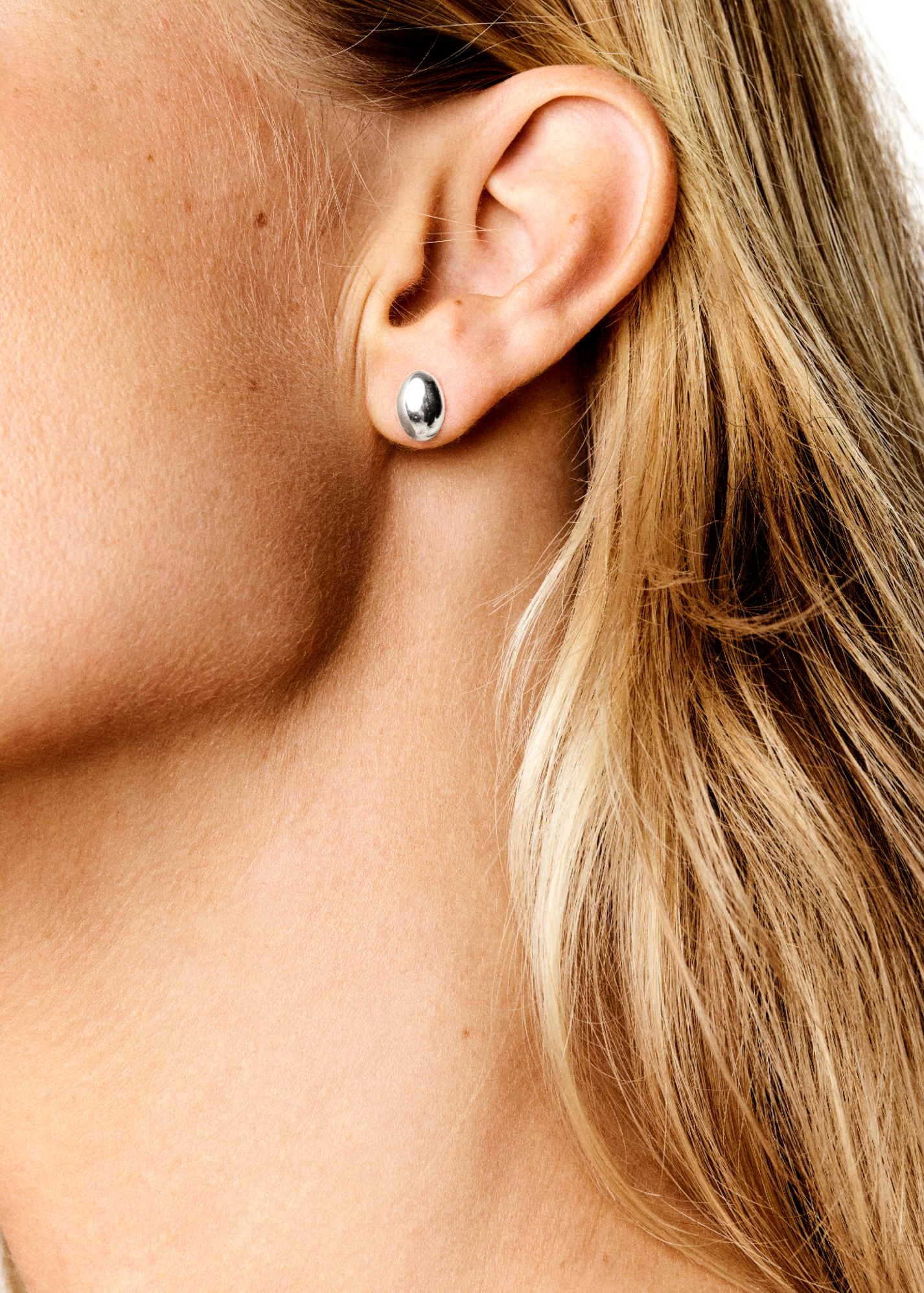 Close-up image of a person's ear adorned with a small, rounded silver stud earring from the LIÉ STUDIO Luna Earrings by Lie Studio. The person has blonde hair.