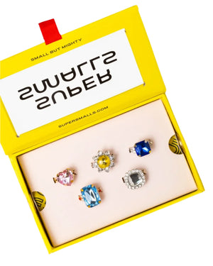 A yellow Super Smalls box labeled "SMALL BUT MIGHTY" holds the Power Lunch Ring Set—five colorful, gem-like rings displayed on a cream insert.